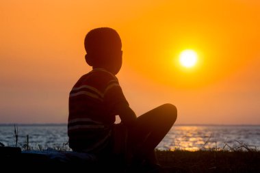 Sakat bir çocuk nehirde oturup gün batımını seyrediyor. Hüzünlü bir günün sonu.