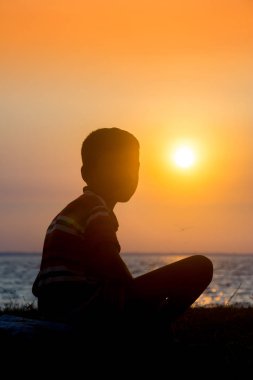 Sakat bir çocuk nehirde oturup gün batımını seyrediyor. Hüzünlü bir günün sonu.