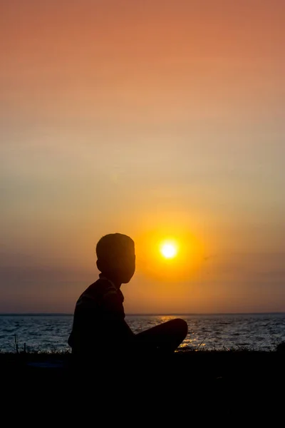 A crippled child sitting at the river watching the sunset. A day ending Sad story.