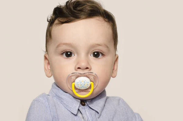 Retrato de um menino bonito olhando para a câmera com uma chupeta na boca . — Fotografia de Stock