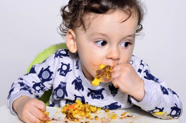 Bir yaşındaki çocuk şut pasta bir dilim kirli elde tek başına yemek.
