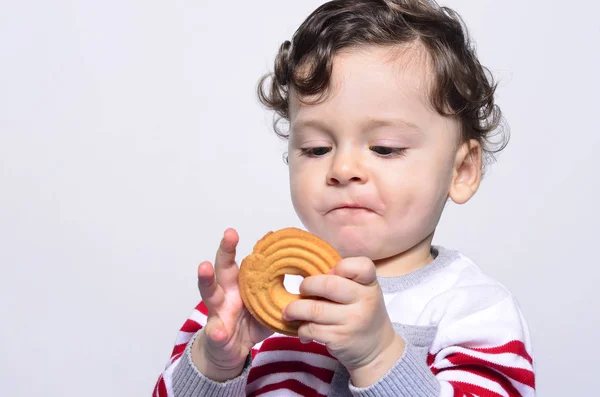 Ritratto di un bambino carino che mangia un biscotto guardandolo curiosamente . — Foto Stock