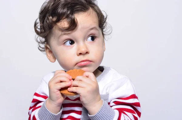 Retrato de um bebê bonito comendo um biscoito olhando para cima curioso . — Fotografia de Stock