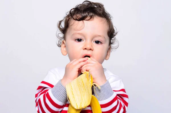 Retrato de un lindo bebé comiendo un plátano . — Foto de Stock