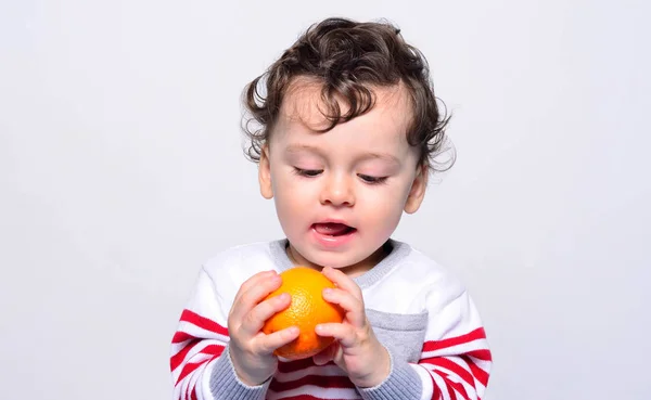 Retrato de un bebé lindo anhelando una naranja . — Foto de Stock