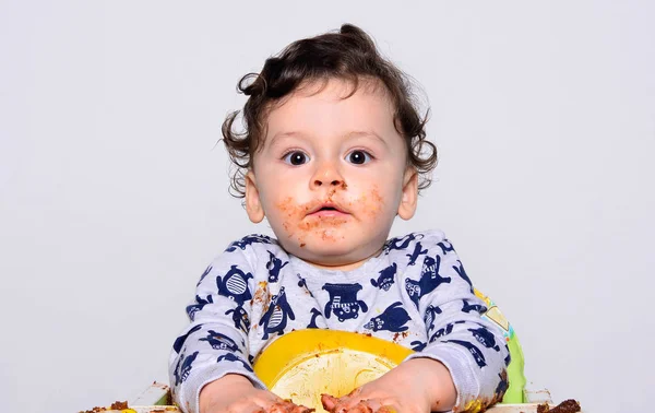 Un bambino di un anno che mangia una fetta di torta di compleanno smash da solo.Bambino che si comporta sorpreso cercando di nascondere il suo pasticcio . — Foto Stock