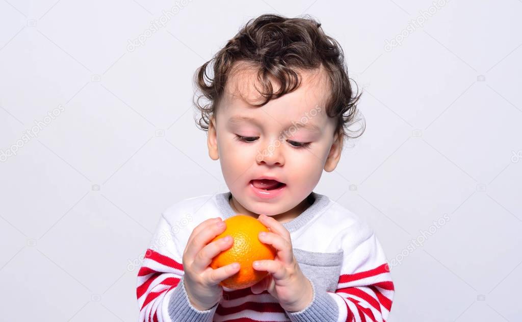 Portrait of a cute baby craving an orange. 