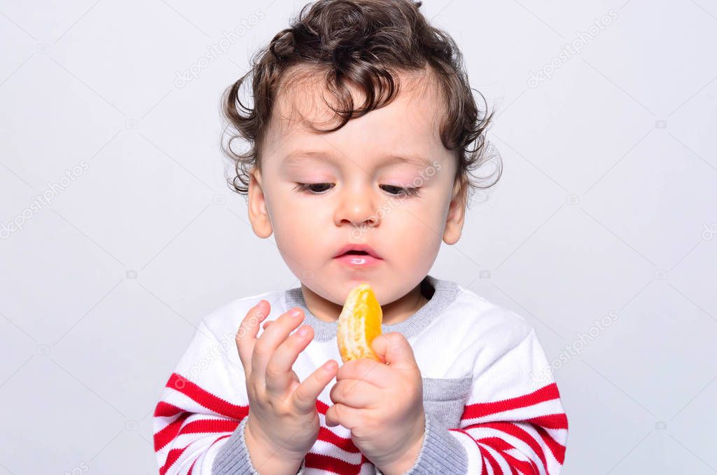 Portrait of a cute baby eating orange. 