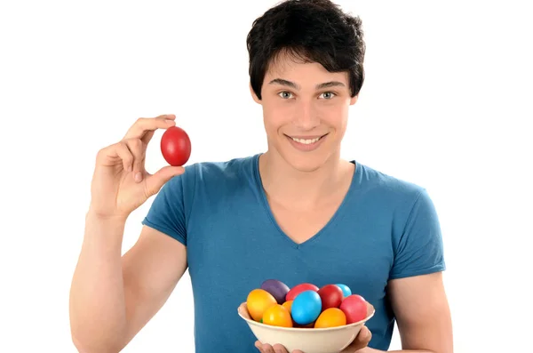 Bonito homem segurando um ovo de Páscoa vermelho e uma cesta com ovos tingidos coloridos . — Fotografia de Stock