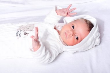 Bebek tulumu giyerek yatakta yatan tatlı bir erkek bebek. Yeni doğmuş bebek beyaz çarşafta yatıyor..