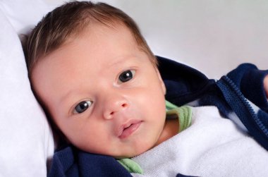 Kameraya bakan sevimli bir erkek bebeğin portresi. Yeni doğmuş bebek beyaz çarşafta yatıyor..