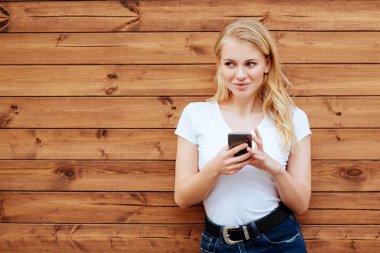 Çekici kadın ayakta ahşap duvar arka plan karşı cep telefonu ile gülüyor