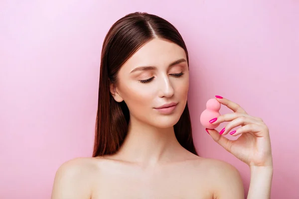 Grappig meisje het houden van roze spons in de buurt van haar gezicht. Portret van jong meisje op roze achtergrond. — Stockfoto