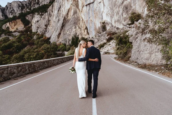 Joven pareja recién casada, novia y novio besándose, abrazándose a la vista perfecta de las montañas —  Fotos de Stock