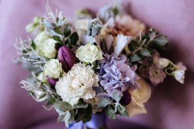 Zengin bir demet pembe şakayık ve leylak çiçekleri, cam vazoda yeşil yaprak.