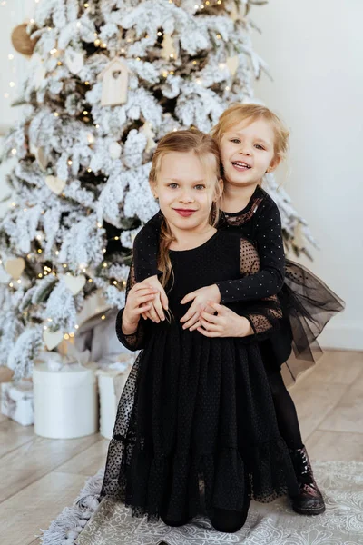 Dwa słodkie urocze siostrzyczki w pobliżu choinki w przytulnym salonie. — Zdjęcie stockowe