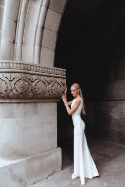 Güzel şık sarışın gelin eski kale duvarının yanında poz veriyor.