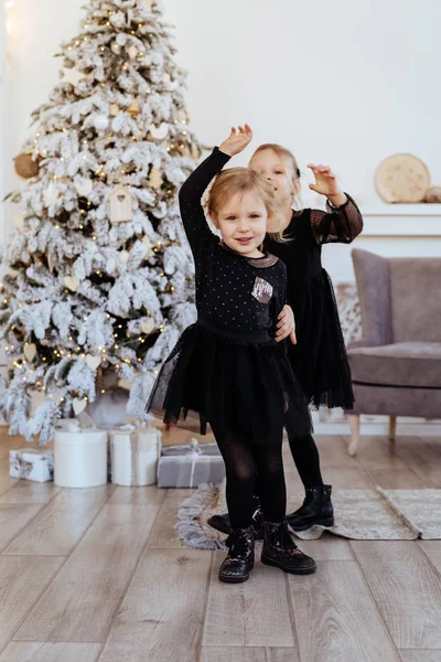 Dos monas adorables hermanitas cerca del árbol de Navidad en la acogedora sala de estar . — Foto de Stock