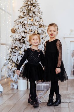 İki sevimli kız kardeş, Noel ağacının yanında, rahat oturma odasında..