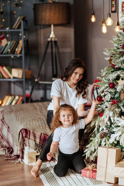 Mamma och ett barn på en säng mot bakgrund av ett nytt år julgran — Stockfoto