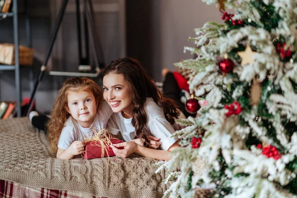 Mamma och ett barn på en säng mot bakgrund av ett nytt år julgran — Stockfoto