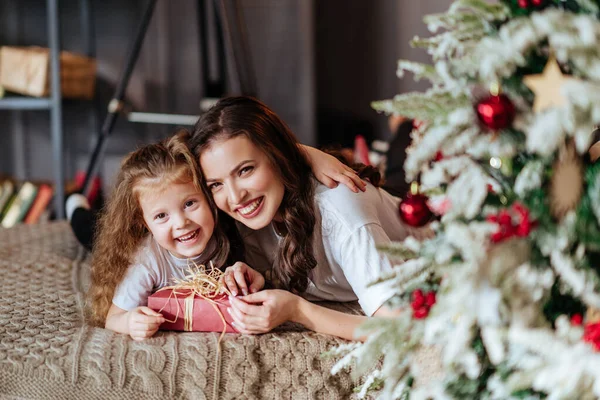 Mamma och ett barn på en säng mot bakgrund av ett nytt år julgran — Stockfoto