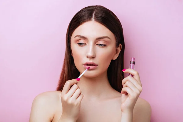 Mooie jonge vrouw met lippenstift op roze achtergrond — Stockfoto