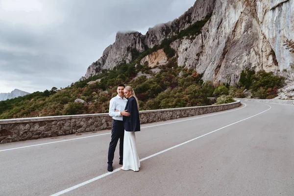 Joven pareja recién casada, novia y novio besándose, abrazándose a la vista perfecta de las montañas —  Fotos de Stock