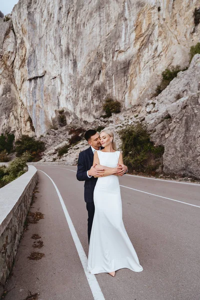 Joven pareja recién casada, novia y novio besándose, abrazándose a la vista perfecta de las montañas — Foto de Stock