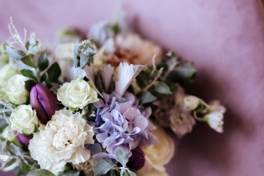 Zengin bir demet pembe şakayık ve leylak çiçekleri, cam vazoda yeşil yaprak.