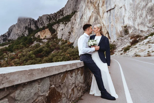 Joven pareja recién casada, novia y novio besándose, abrazándose a la vista perfecta de las montañas — Foto de Stock