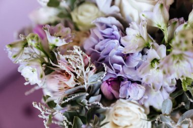 Zengin bir demet pembe şakayık ve leylak çiçekleri, cam vazoda yeşil yaprak.