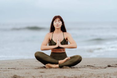 Yoga kumsalındaki kadın okyanusta poz veriyor.