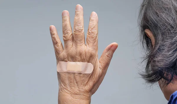 Ältere Frau klebt Verband an ihrer Hand — Stockfoto