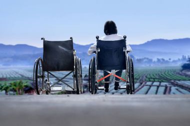 Elderly woman with empty wheelchair standing together clipart