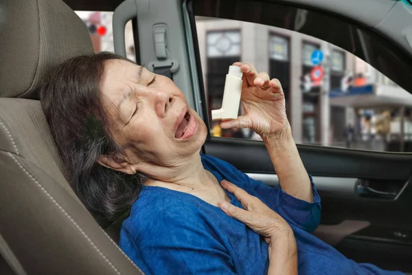 Femme âgée étouffant et tenant un spray d'asthme à l'intérieur de la voiture sur le chemin — Photo