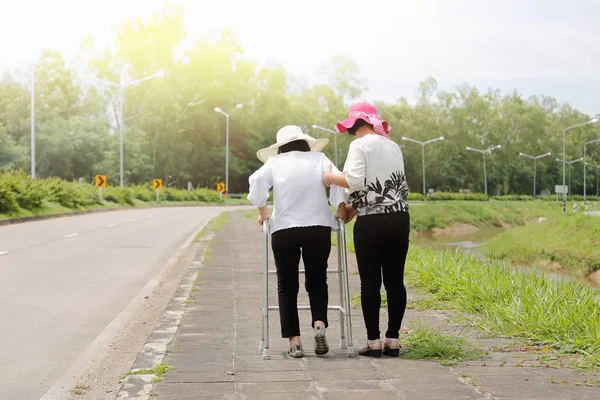 Dochter verzorgen bejaarde vrouw lopen op straat in sterke zon — Stockfoto