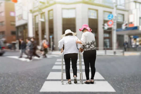 Hija cuidar anciana caminando a través de la calle en fuerte sol — Foto de Stock