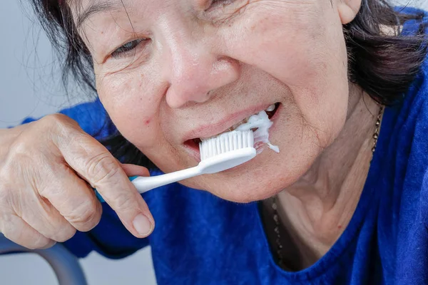 Азиатская пожилая женщина пытается использовать зубную щетку, дрожь в руке. Здоровье зубов — стоковое фото