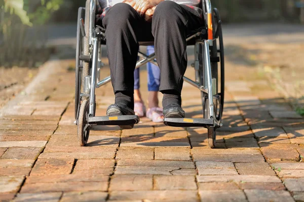 Elderly woman in wheelchair walking with caregiver — Stock Photo, Image