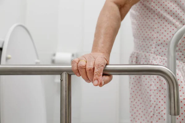 Elderly woman holding on handrail in toilet. — Stock Photo, Image