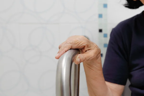 Bejaarde vrouw houden over de leuning in badkamer. — Stockfoto