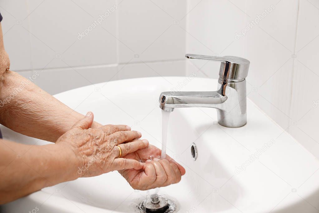 Elderly woman washes hand in bathroom