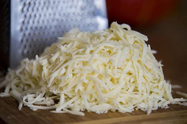 Shredded mozzarella cheese on a cutting board with a grater — Stock Photo, Image