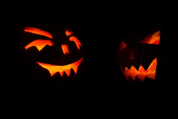 Zwei geschnitzte Gesicht von Kürbis glühend auf halloween schwarzem Hintergrund — Stockfoto