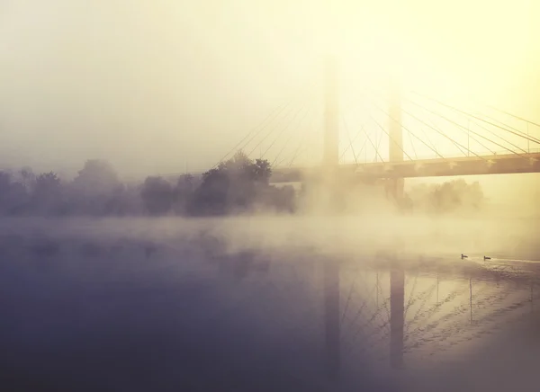 Nebel bedeckt Fluss und Brücke bei Sonnenaufgang — Stockfoto