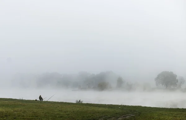 Fiskare man fiske på en flodbank i dimmiga dimmig soluppgång — Stockfoto