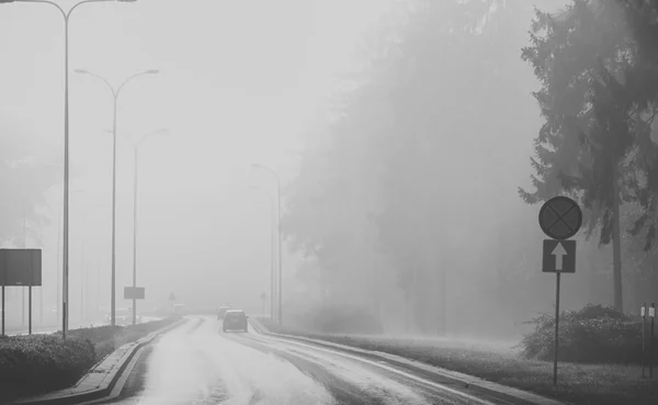Samochody we mgle. Zła pogoda i niebezpieczny ruch samochodowy na drodze. czarno-białe — Zdjęcie stockowe