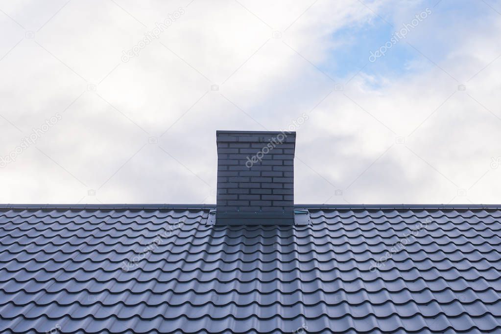 Roof with ceramic tile chimney against cloudy blue sky