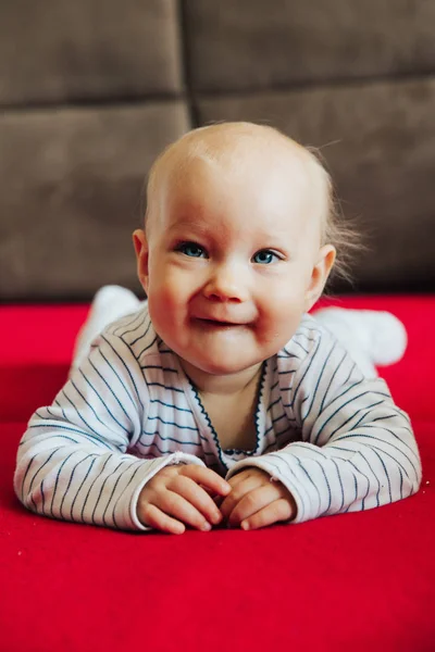 Nieuwsgierig baby meisje liggend op bed, glimlachende front view — Stockfoto